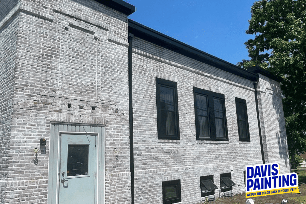 A two-story brick building with black-trimmed windows and a light gray door. The facade features a weathered brick design, reminiscent of old church paintings. On the bottom right, there is a "Davis Painting" logo with the slogan "We Put the Color Back in Your Life!