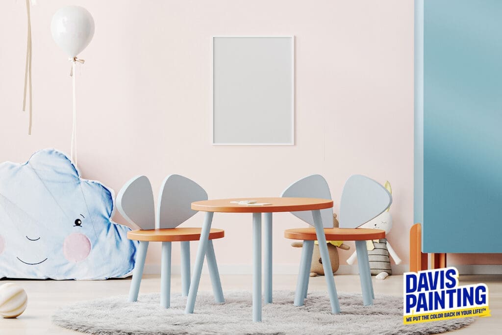 A child's playroom features a small round wooden table with two matching chairs, each with pastel blue accents. A large, plush cloud-shaped pillow sits on the floor beside a balloon and toys. A "Davis Painting" logo is in the bottom right corner, renowned for its excellence in historical restoration.