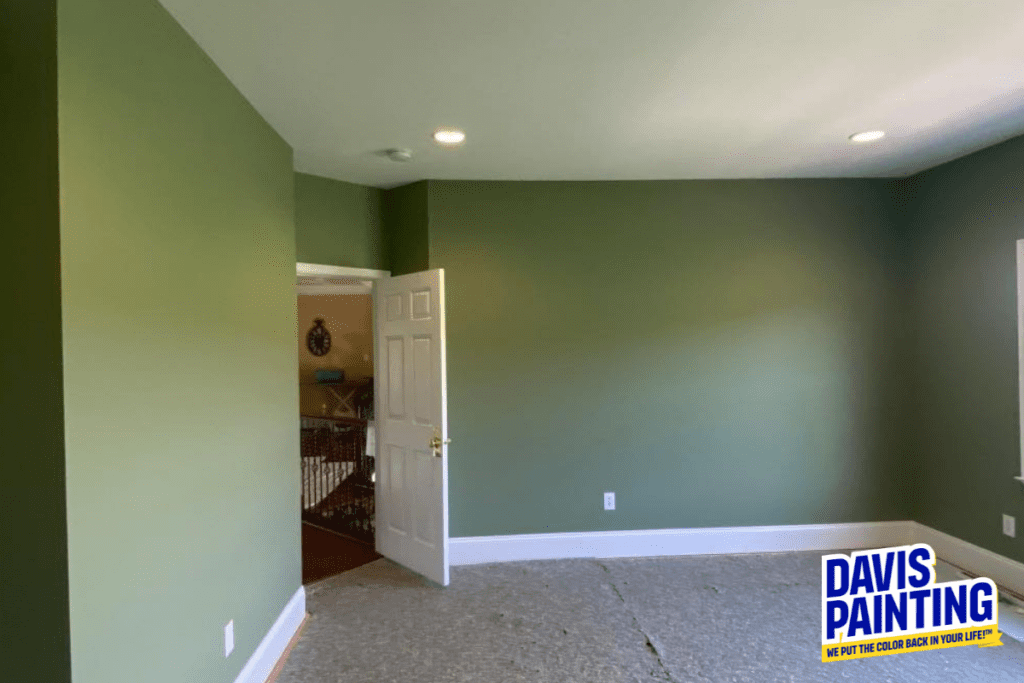 A freshly painted empty room with green walls and a light ceiling. The floor is bare, awaiting installation. An open door reveals a glimpse of an adjacent room. A "Davis Painting" logo is displayed in the bottom right corner.