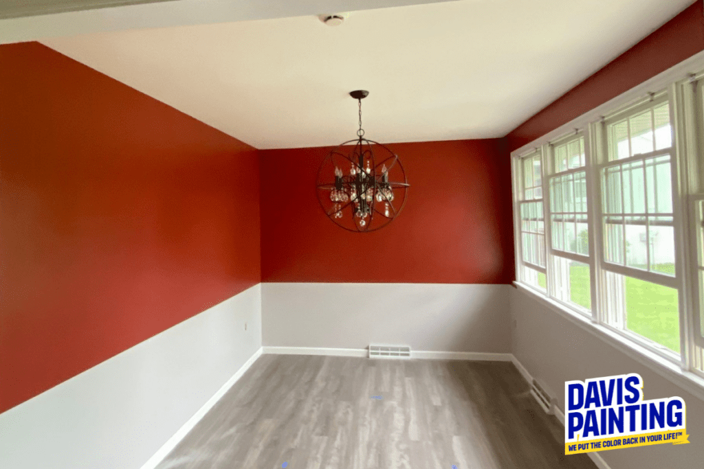 A freshly painted room with red and white walls, a modern chandelier, and wooden flooring. Large windows on the right let in natural light. Logo in the bottom right corner says "Davis Painting.