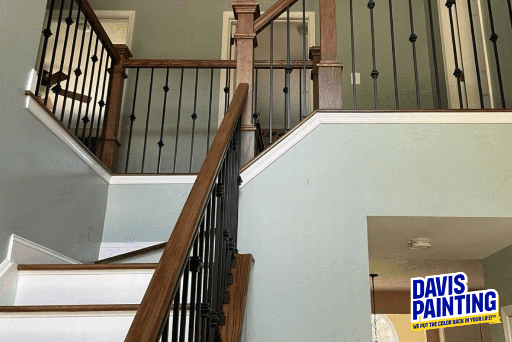 A staircase with wooden handrails and black metal balusters is shown. The walls are painted in a light blue-green color. A company logo for Davis Painting is in the bottom right corner.