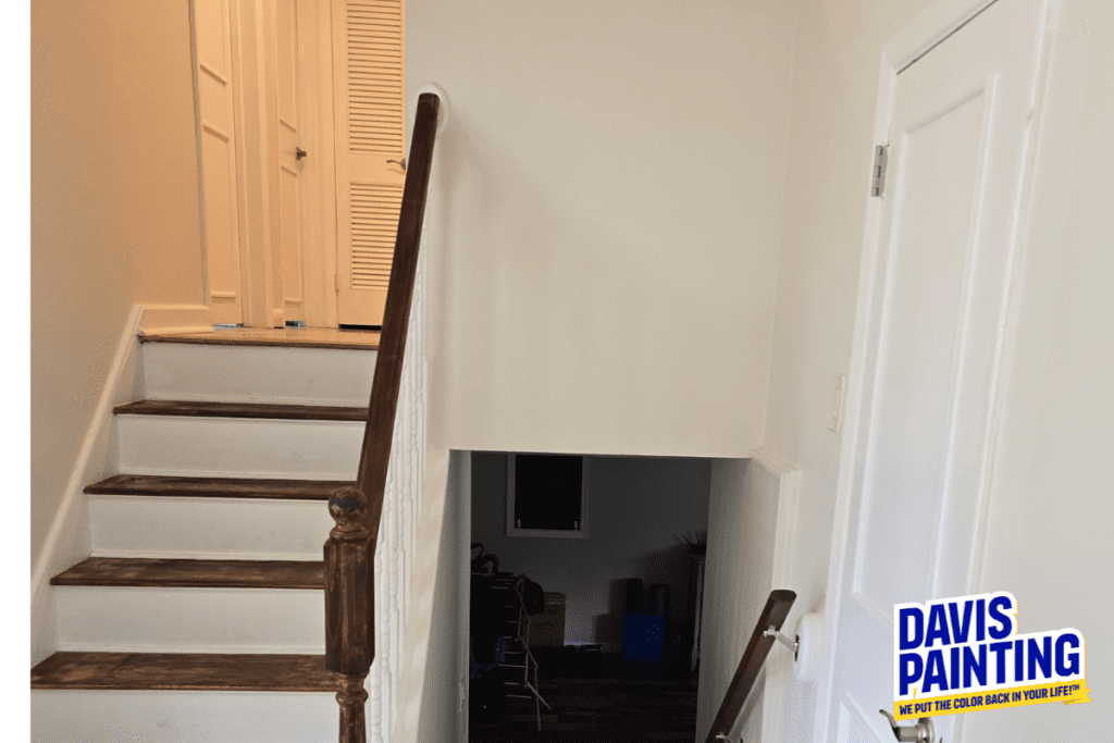 View of an indoor stairway with wooden steps and white railing, featuring a landing leading upstairs and downstairs. The wall has a logo "Davis Painting" at the bottom right.