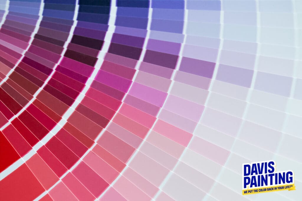 A spectrum of colored paint swatches fans out from reds to blues on a white background, showcasing a vibrant palette perfect for interior design. In the bottom right corner, the logo and slogan of Davis Painting proudly stand.