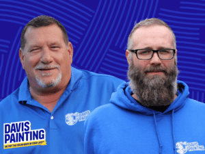 Two men wearing blue Davis Painting shirts pose in front of a textured blue background. One sports a short haircut with a goatee, while the other has a full beard and glasses. The Davis Painting logo is displayed in the corner, highlighting their expertise in cabinet painting vs. replacement.